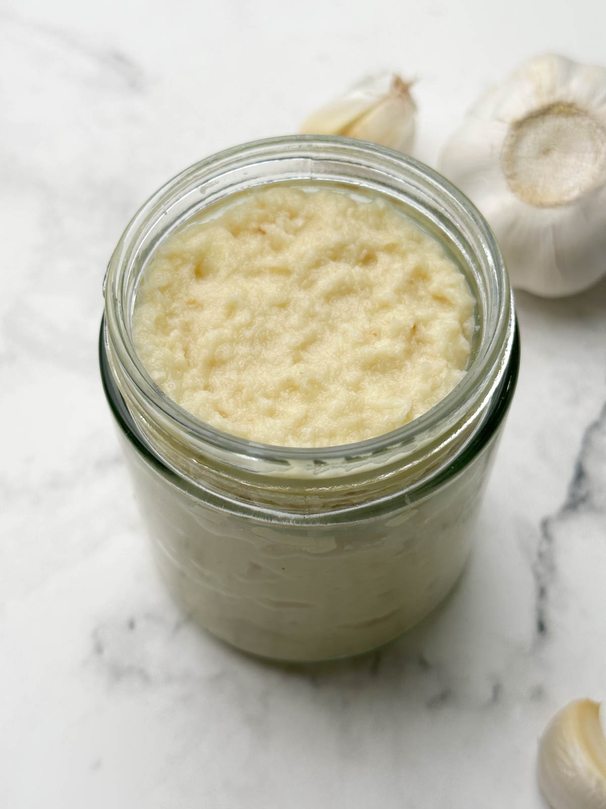 homemade fresh garlic paste in a glass container with garlic bulb on the side