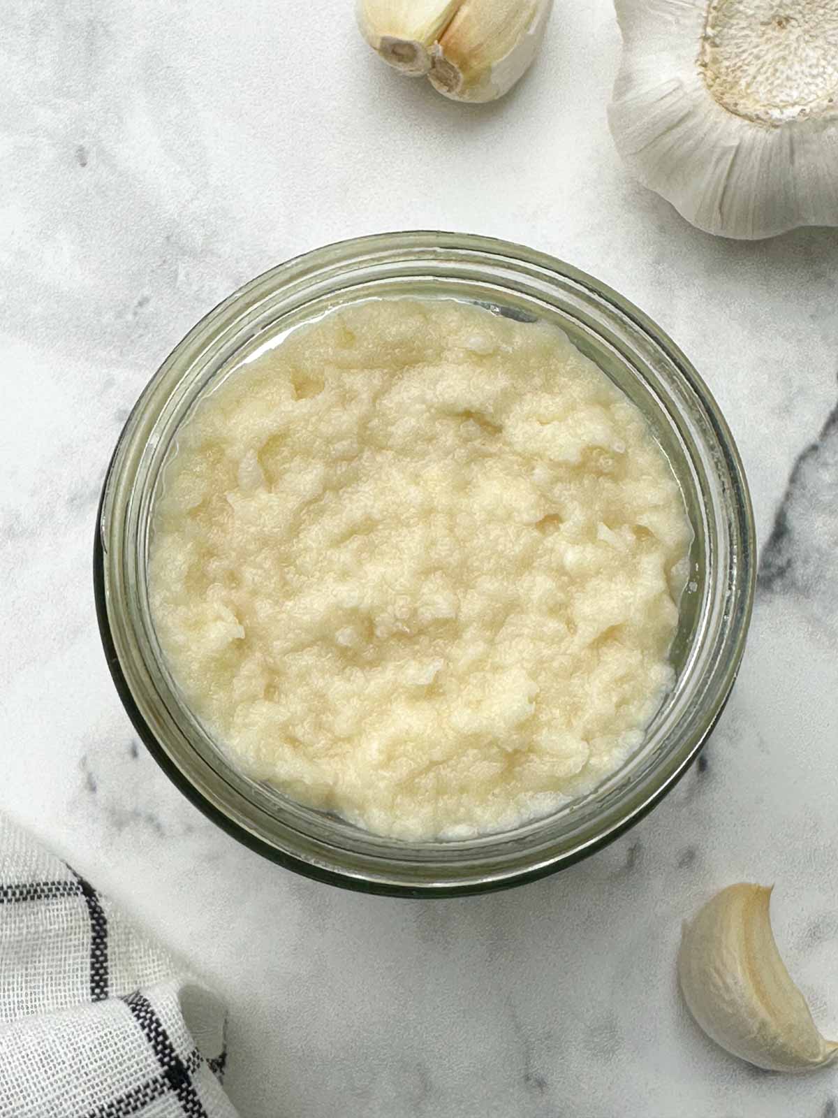 fresh garlic paste in a glass container, with garlic cloves on the side