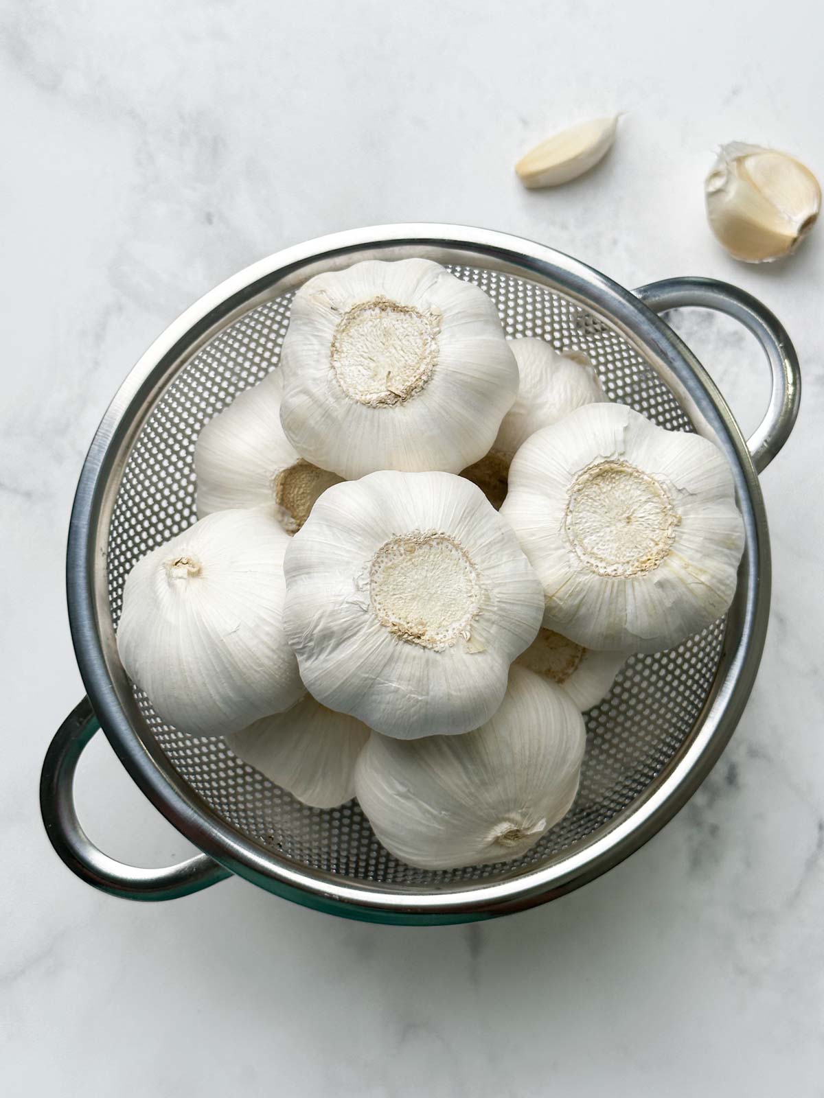 whole garlic bulbs in a mesh container and cloves on the ground