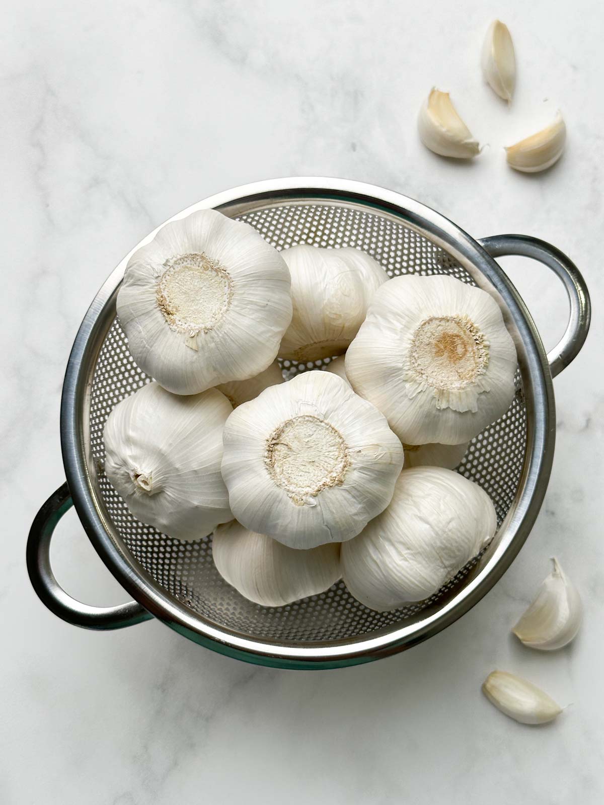 whole garlic bulbs in a mesh container and cloves on the ground