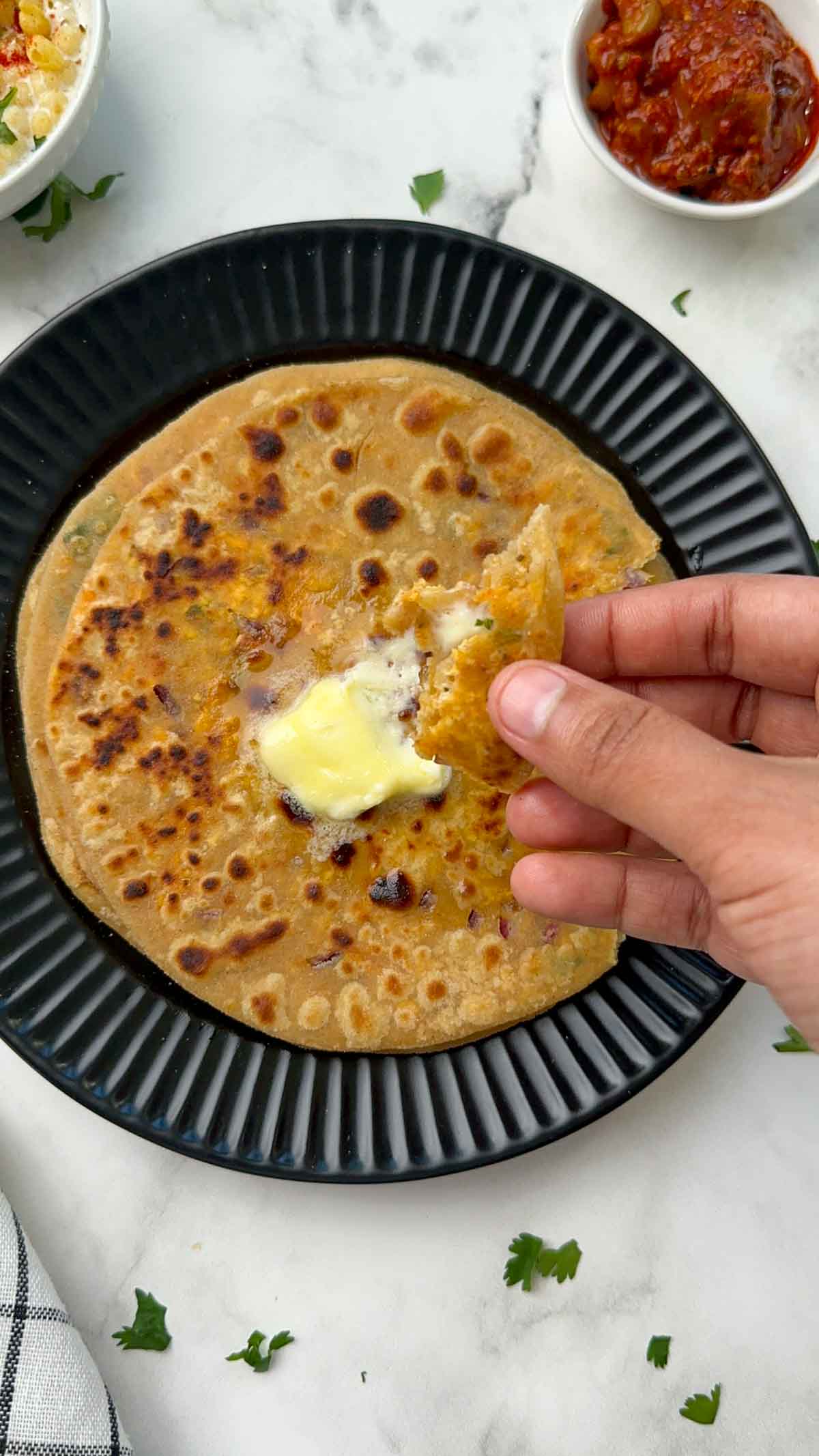 a bite of paneer paratha in the hand with some butter