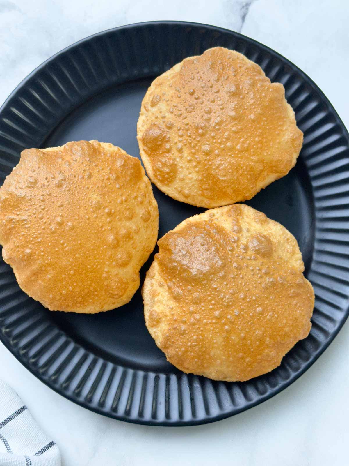 crispy and puffy three puffed indian bread served on a plate