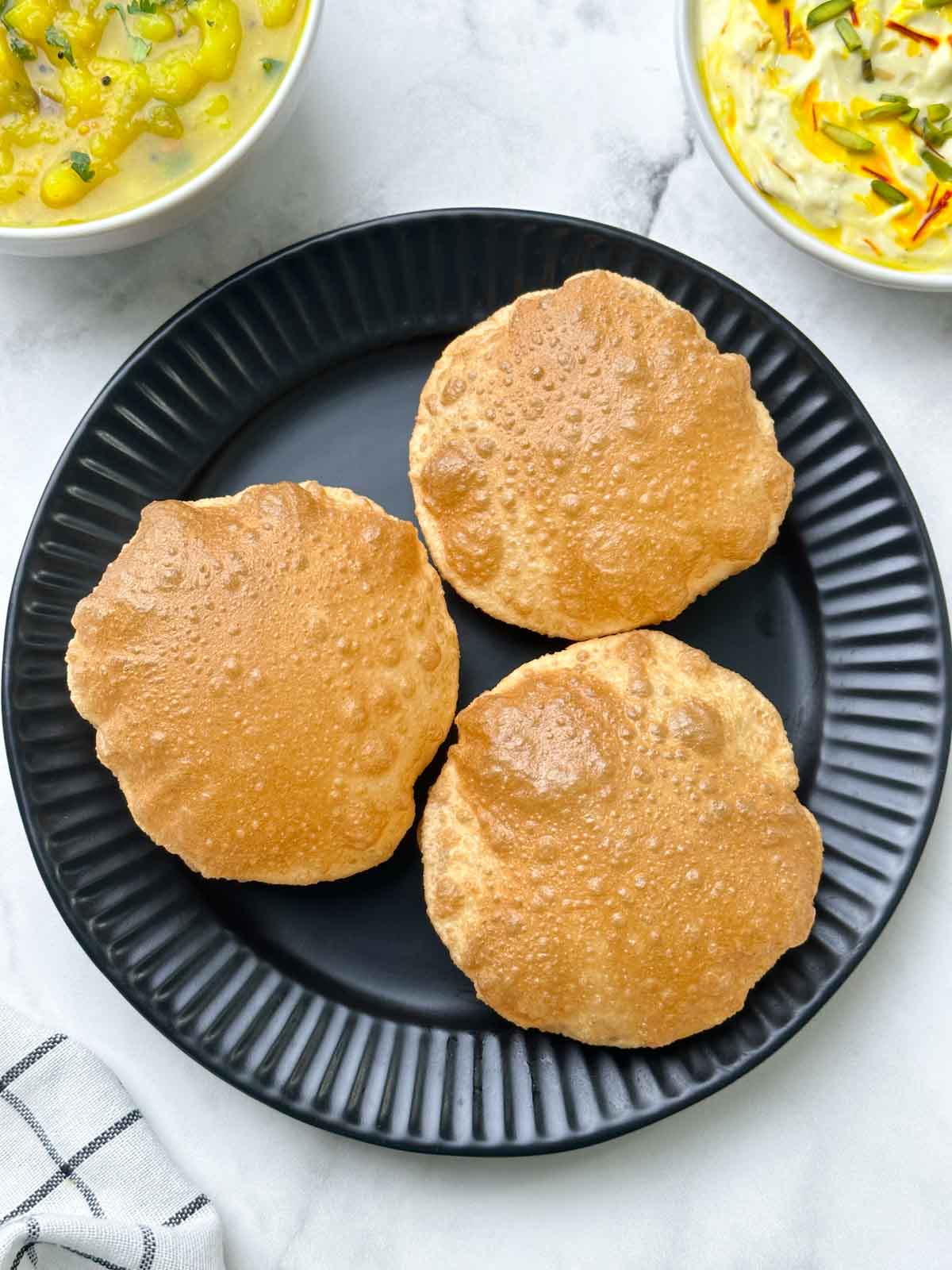 crispy and puffy poori served on a plate with potato sagu and shrikhand on the side