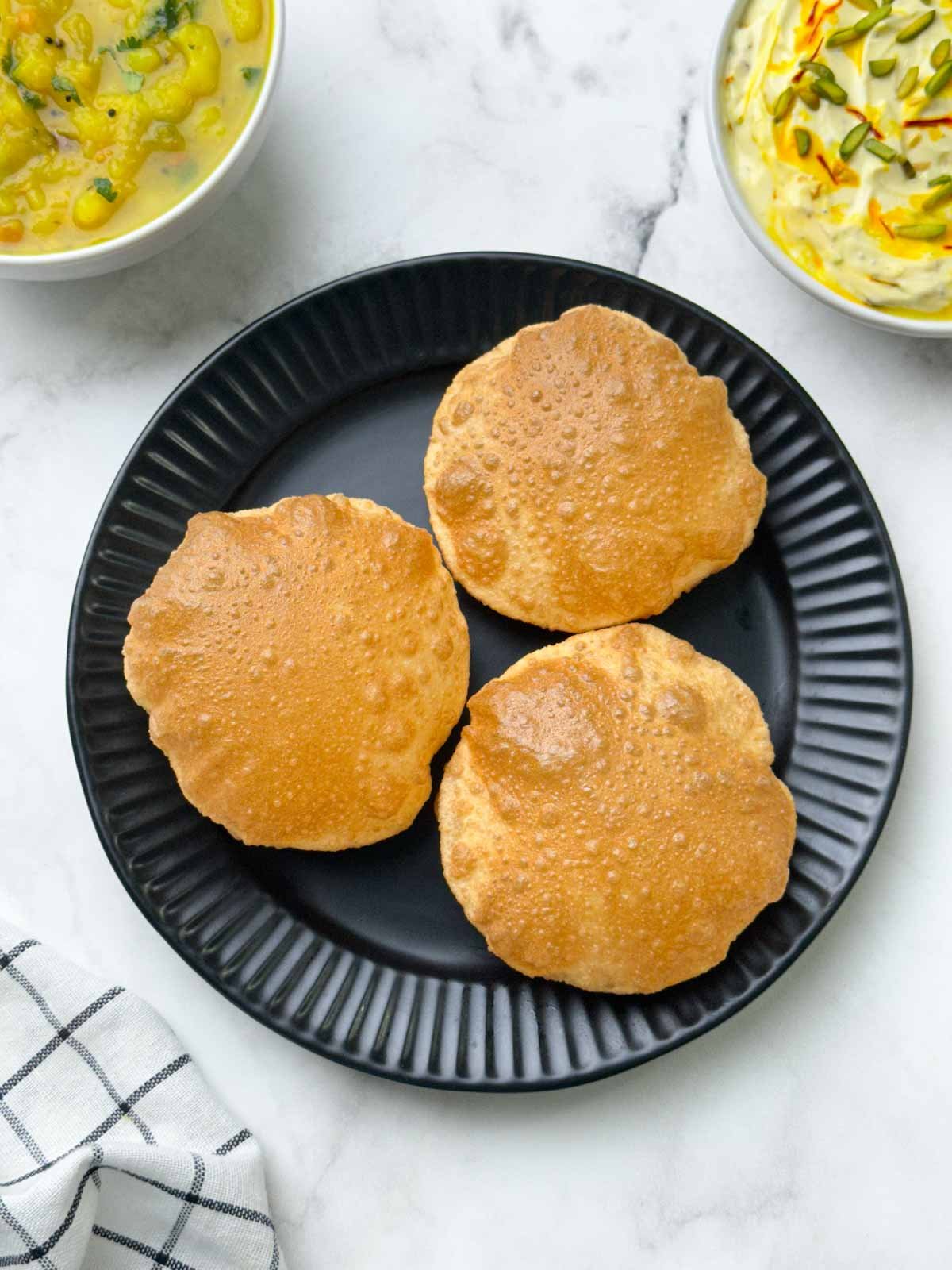 crispy and puffy poori served on a plate with potato sagu and shrikhand on the side