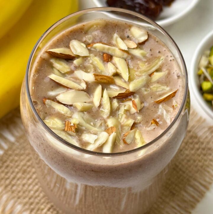 ragi banana and dates smoothie served in a glass topped with almonds with banana, dates and nuts on the side