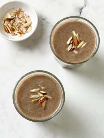 ragi malt served in two glass cups garnished with slivered almonds with nuts on the side