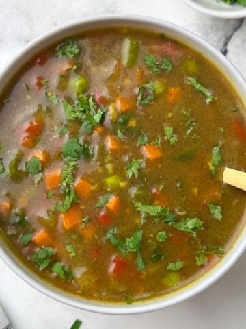 ragi vegetable soup served in a bowl with a spoon and cilantro on the side