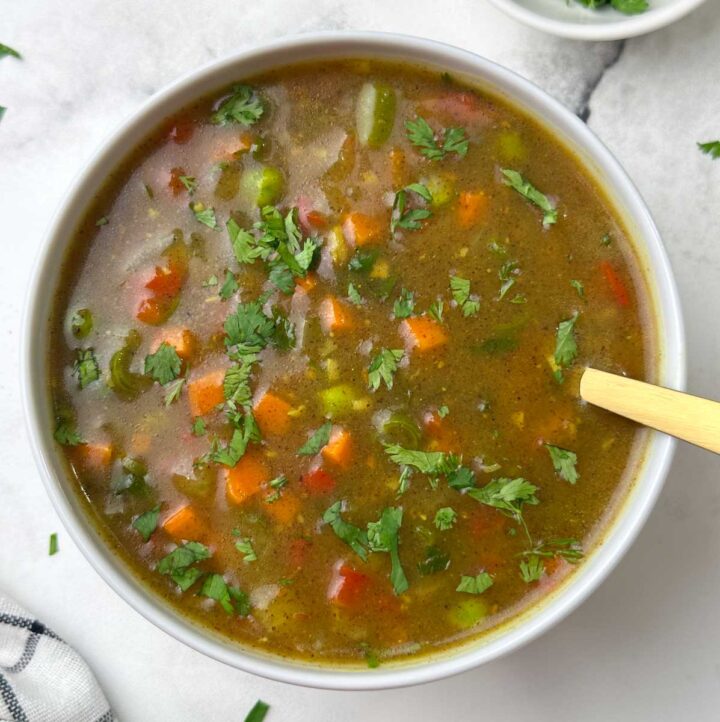 ragi vegetable soup served in a bowl with a spoon and cilantro on the side