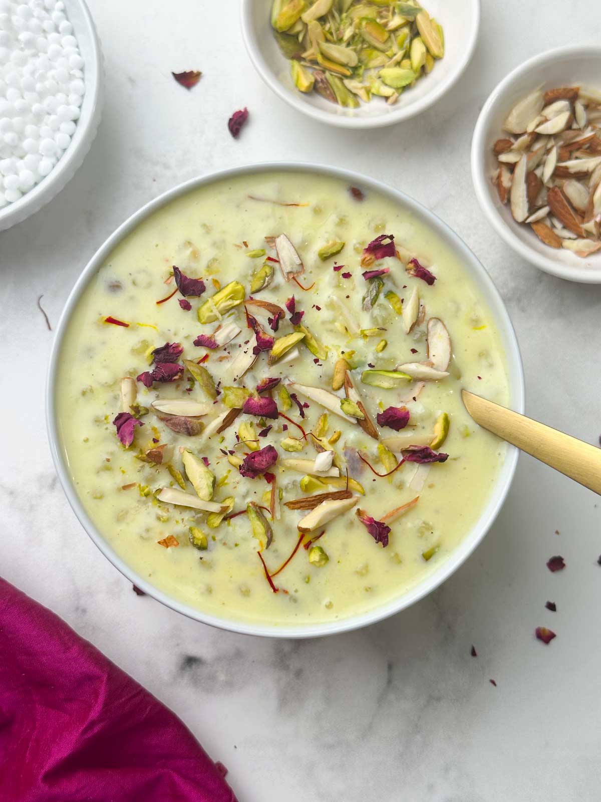 sabudana kheer (sago pudding) served in a bowl with a spoon inside garnished with rose petals and nuts