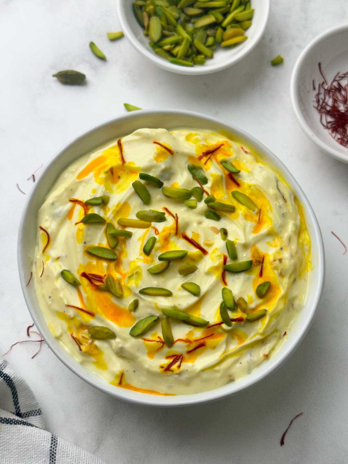shrikhand served in a bowl with poori, pista and saffron strands on the side