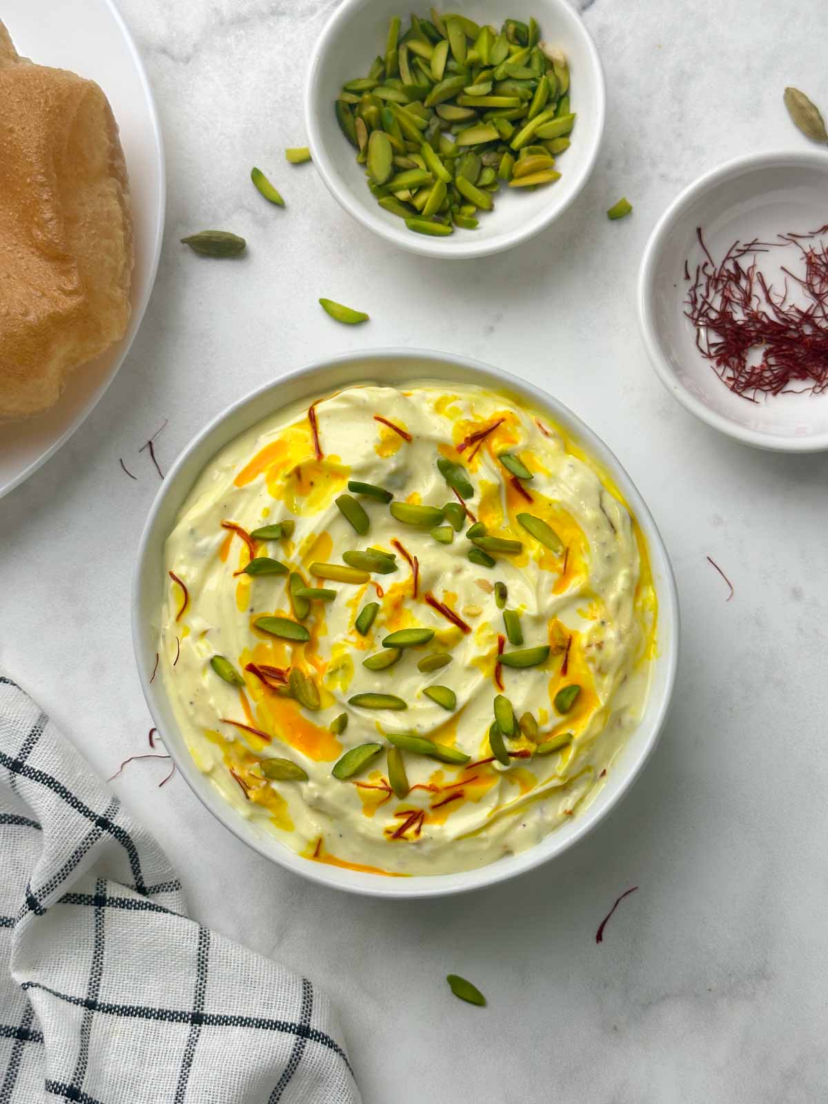 shrikhand served in a bowl with poori, pista and saffron strands on the side