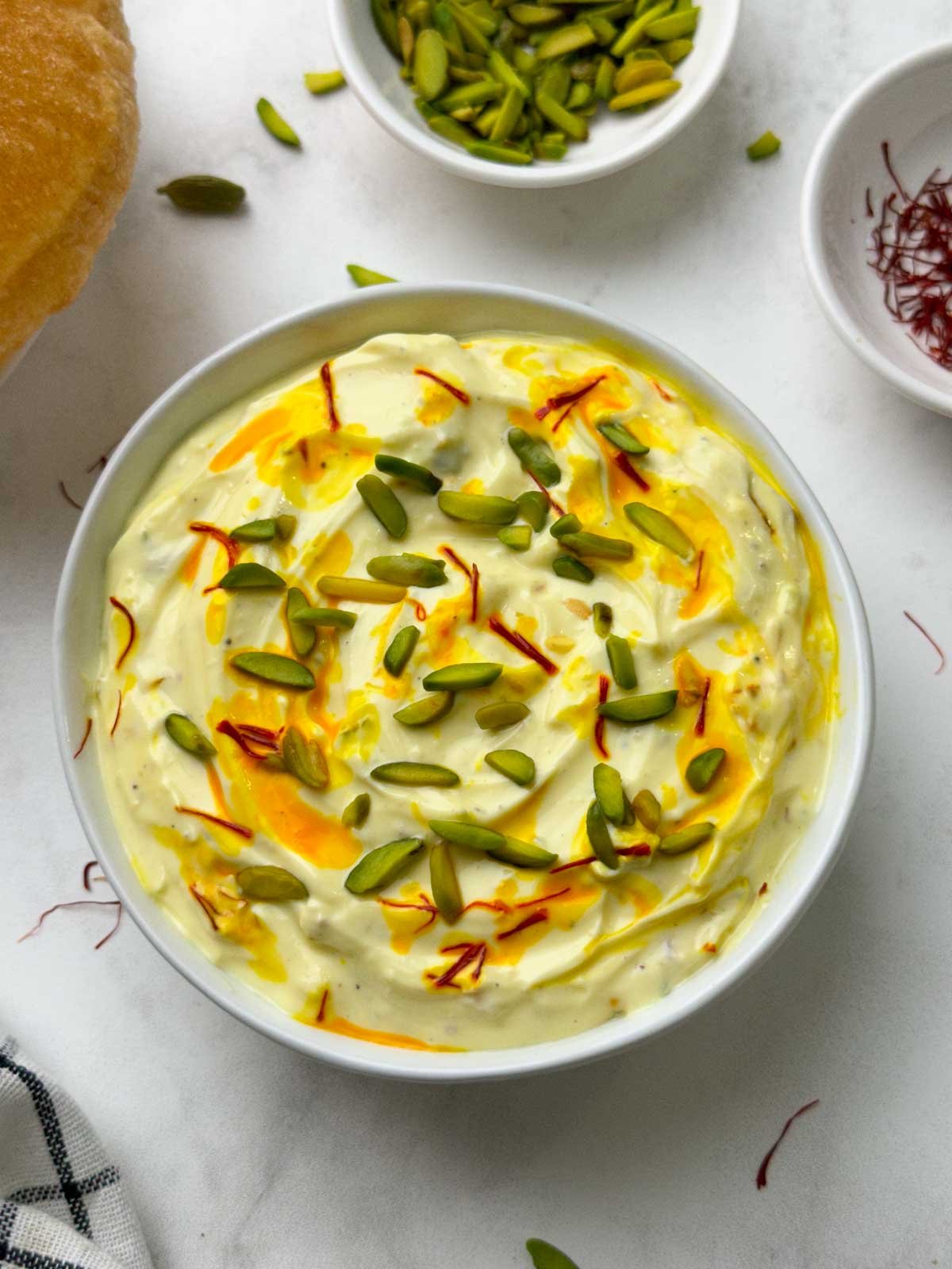 shrikhand served in a bowl with poori, pista and saffron strands on the side