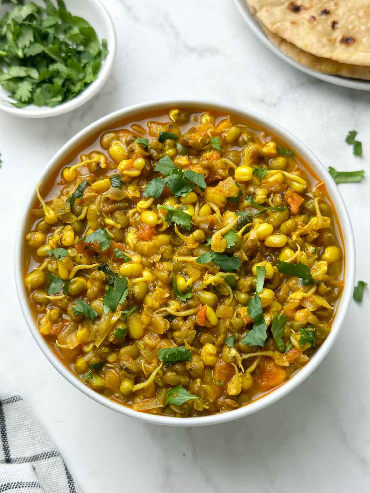sprout moong curry served in a bowl with chapati and coriander leaves on the side