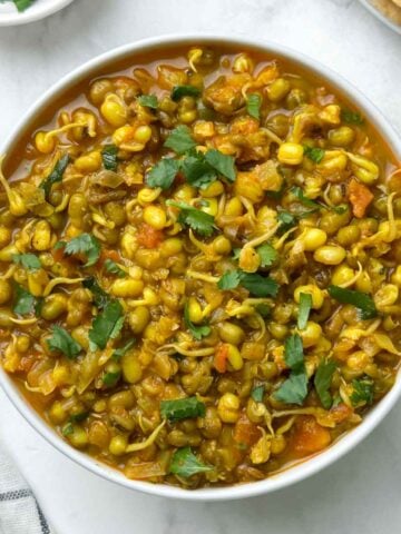 sprout moong curry served in a bowl with chapati and coriander leaves on the side