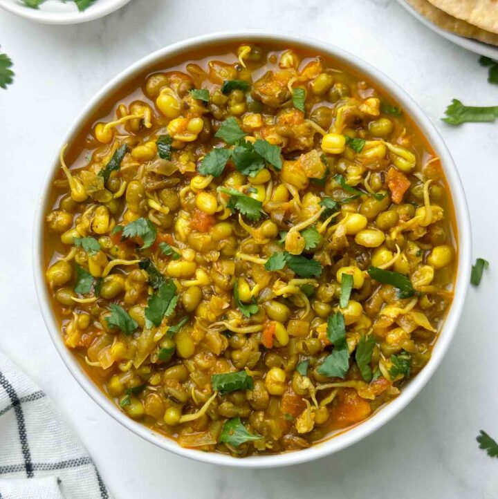 sprout moong curry served in a bowl with chapati and coriander leaves on the side
