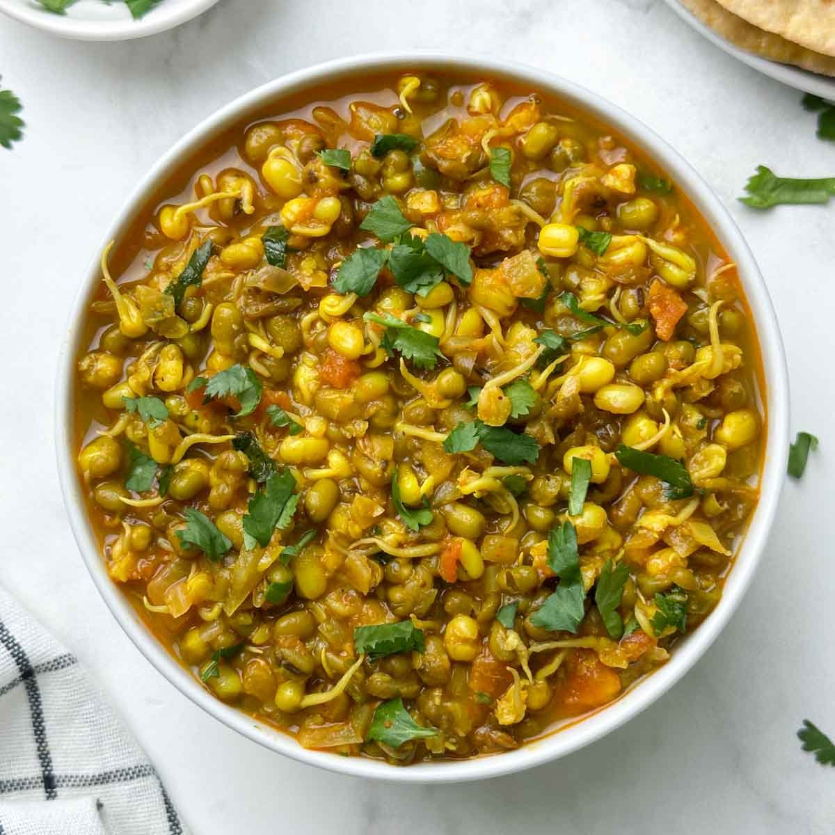 sprout moong curry served in a bowl with chapati and coriander leaves on the side