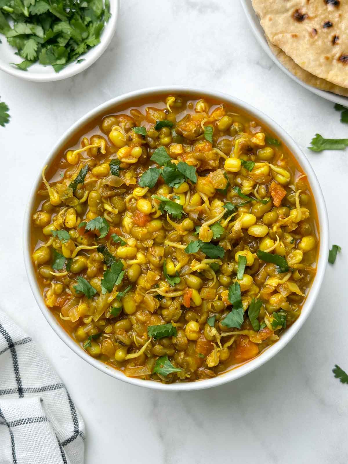 sprout moong curry served in a bowl with chapati and coriander leaves on the side