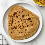 Stack of triangular shape paratha on a white plate with cabbage stir fry on the side.