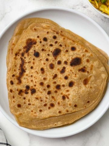 Stack of triangular shape paratha on a white plate with cabbage stir fry on the side.
