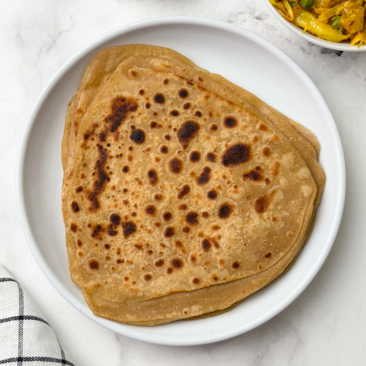 Stack of triangular shape paratha on a white plate with cabbage stir fry on the side.