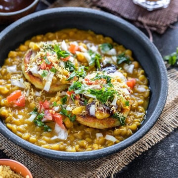 Ragda Patties served in a bowl with chutneys and chai on the side.