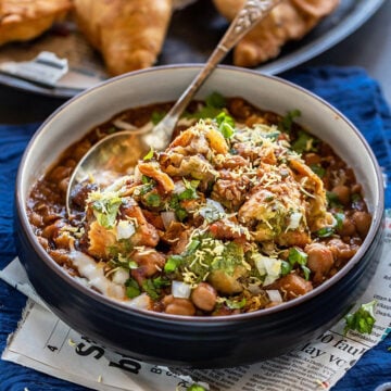 Samosa Chaat served in a bowl with a spoon and whole samosas on the side.