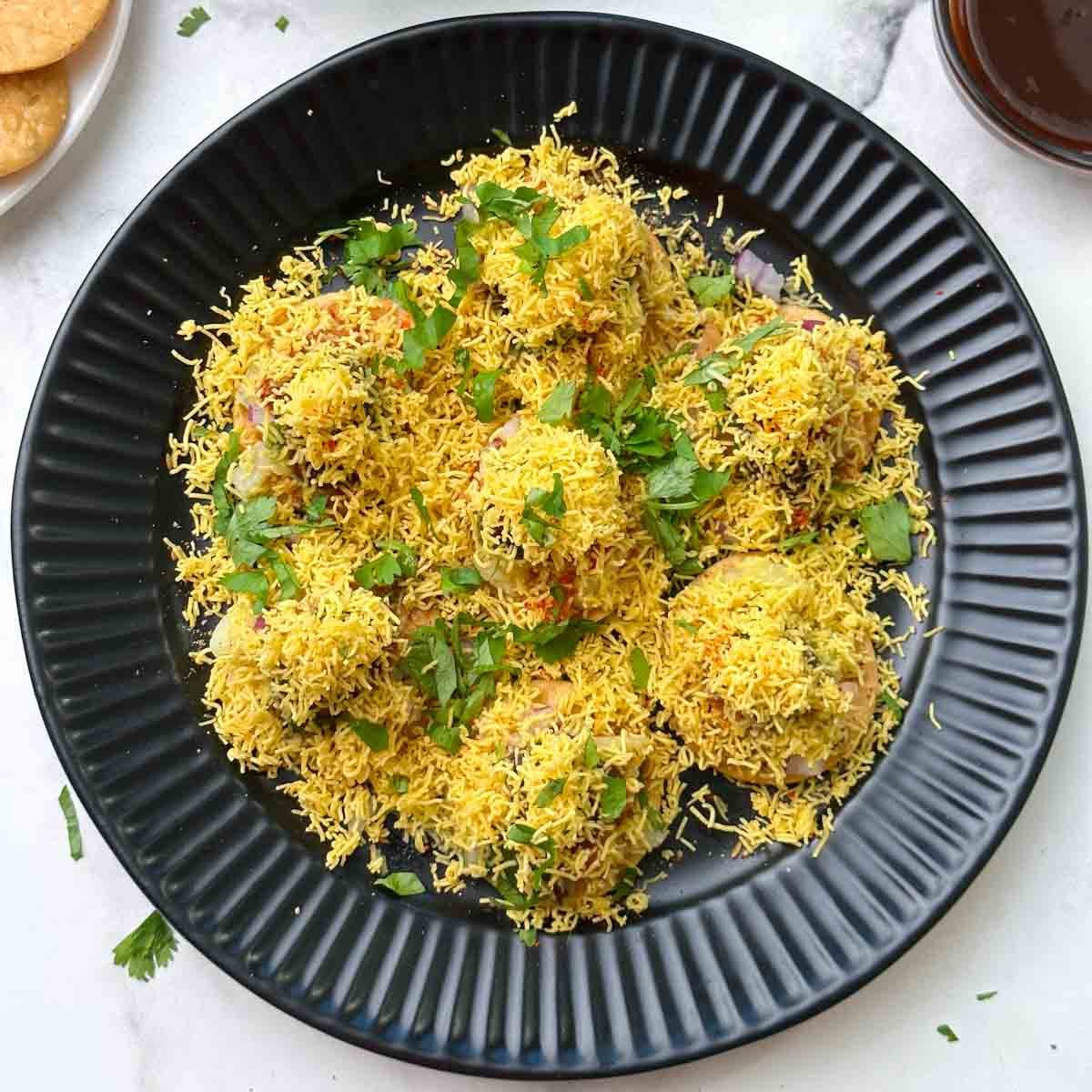 sev puri chaat served on a plate with sev and chutneys on the side