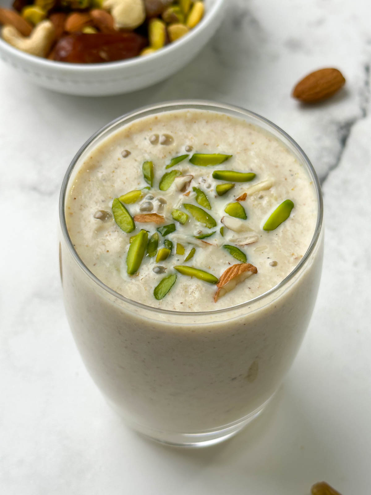 dryfruits milkshake served in a glass garnished with pistachios and mixed dry fruits on the side in a bowl