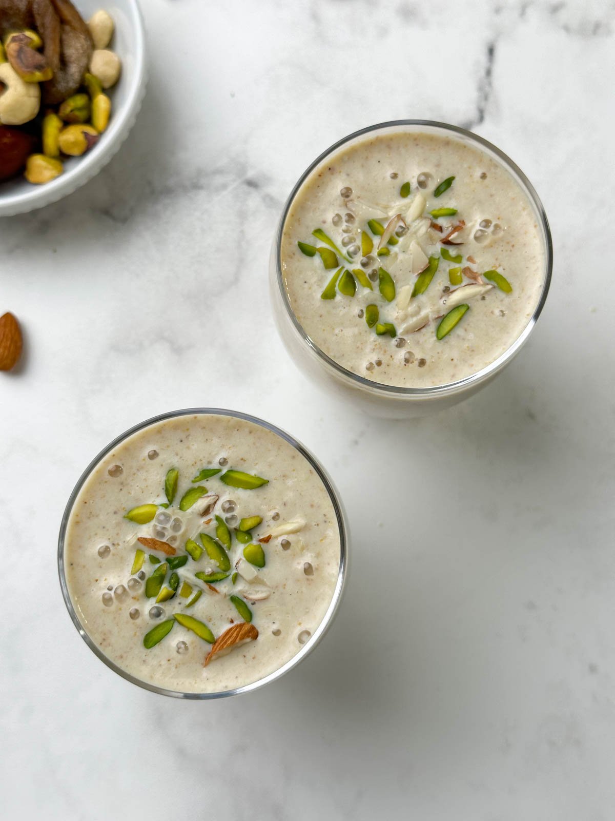 dried fruits milkshake served in a glass garnished with pistachios and mixed dry fruits on the side in a bowl