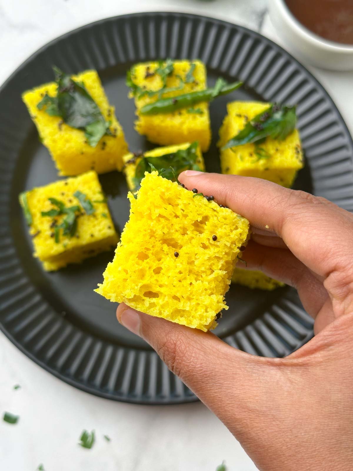 khaman in hand with chutneys on the side