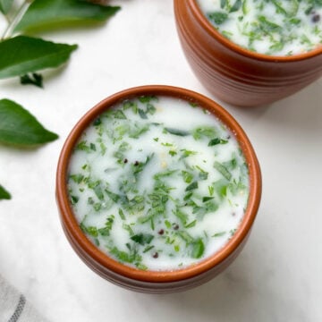 neer mor (neer majjige) served in a serving glass with curry leaves and ginger on the side