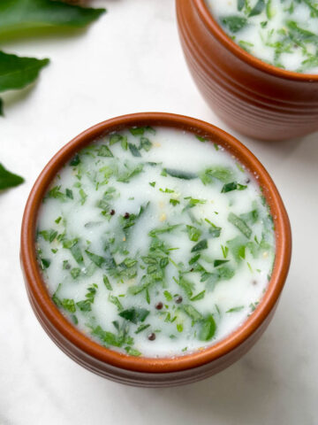 neer mor (neer majjige) served in a serving glass with curry leaves and ginger on the side