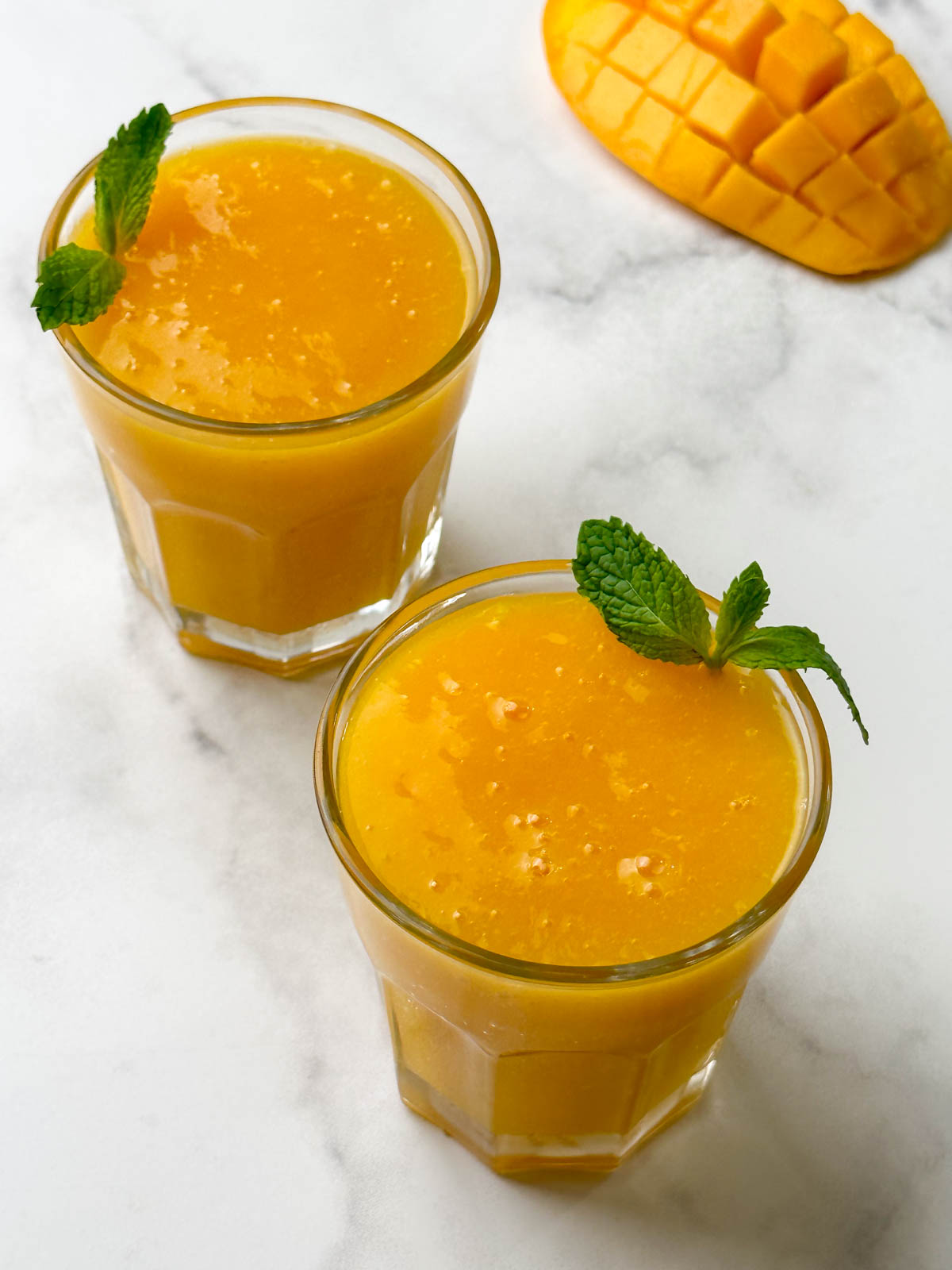 2 glasses with mango juice with mint on the top for garnish