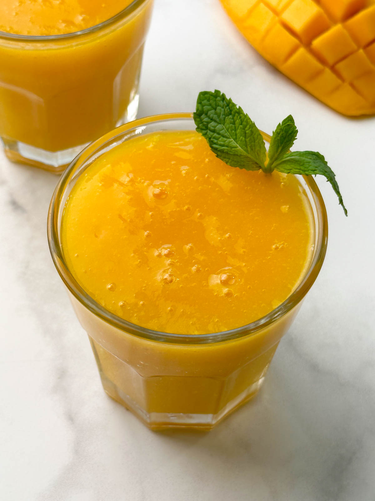mango juice served in 2 glass containers with mint on the top for garnishing