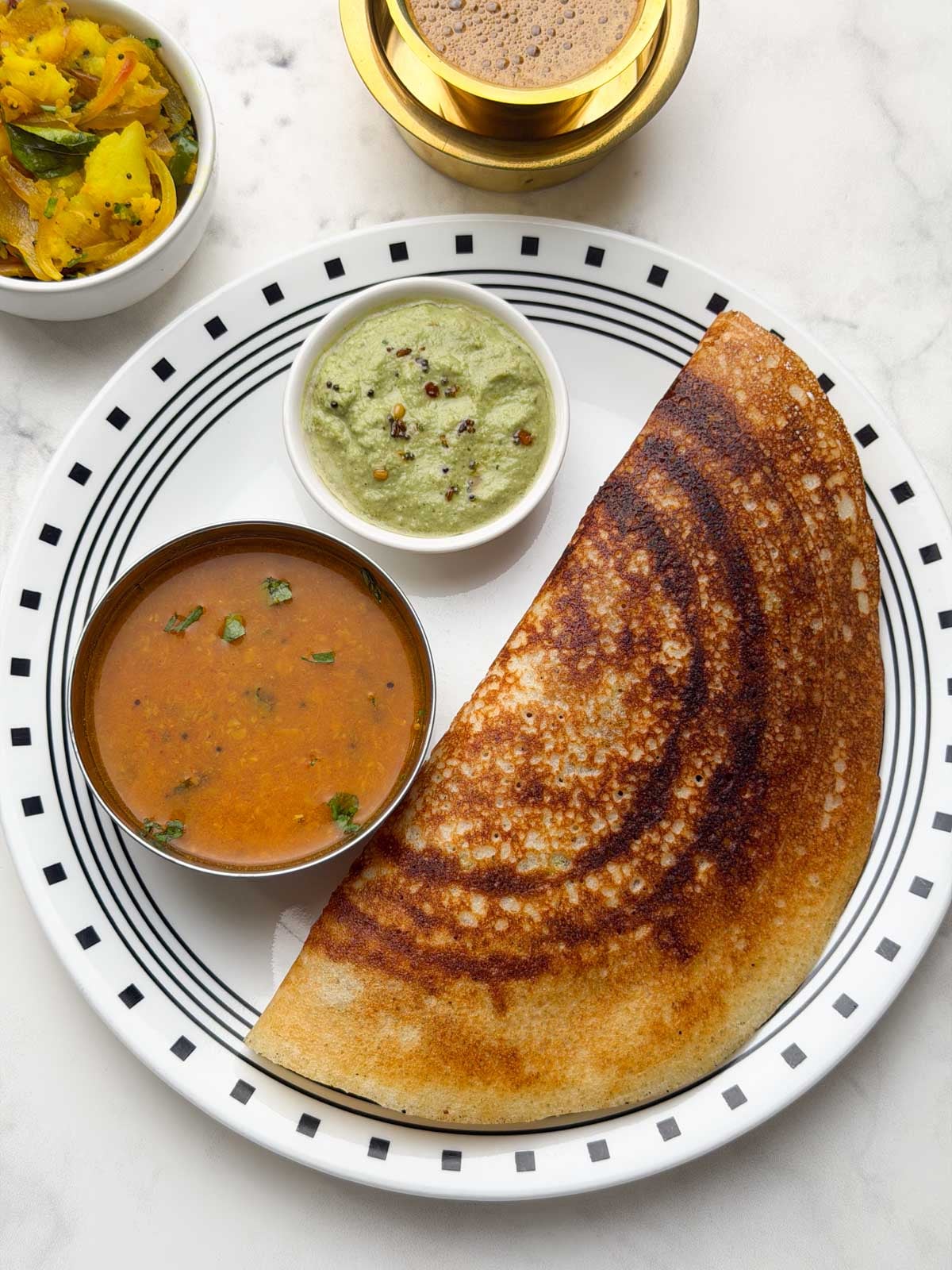 One crispy masala dosa served on a white plate with coriander coconut chutney and sambar and filter coffee and potato masala palya on the side.