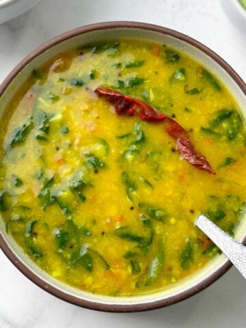 fenugreek (methi) leaves dal with a spoon served in a bowl with rice and cucumber on the side