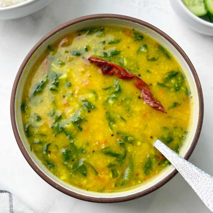 fenugreek (methi) leaves dal with a spoon served in a bowl with rice and cucumber on the side