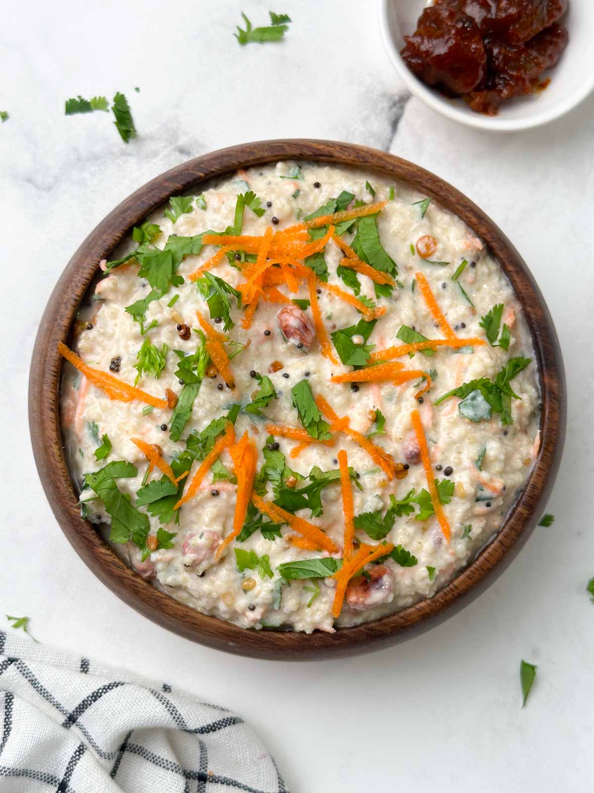 millet curd rice served in a wooden bowl garnished with carrot and coriander leaves with pickle on the side