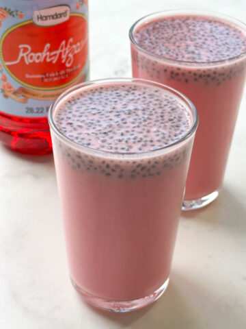 rooh afza milk served in glasses topped with soaked sabja seed and rooh afza syrup bottle on the side
