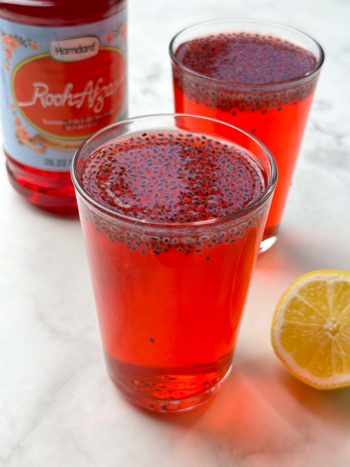 two glasses of rooh afza drink served topped with sabja seeds and rooh afza bottle on the side