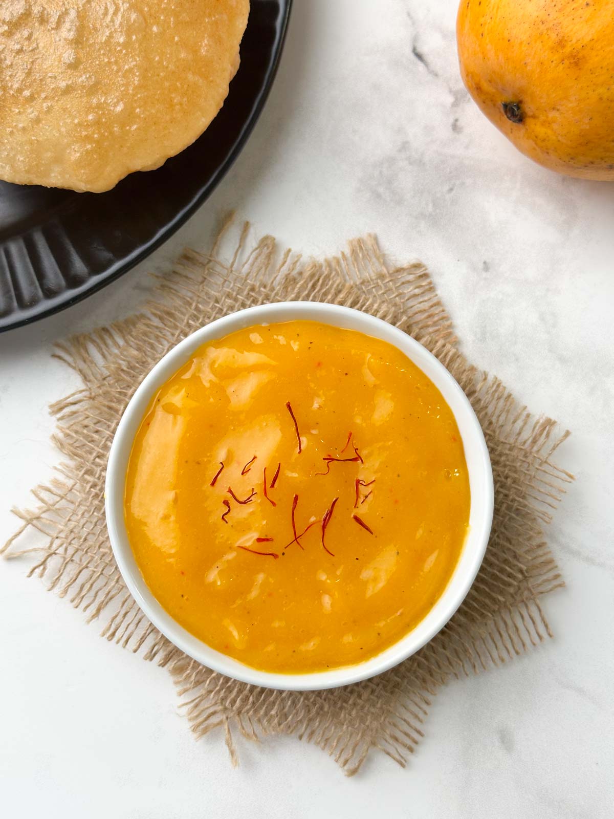 aamras recipe served in a bowl garnished with saffron with poori on the side