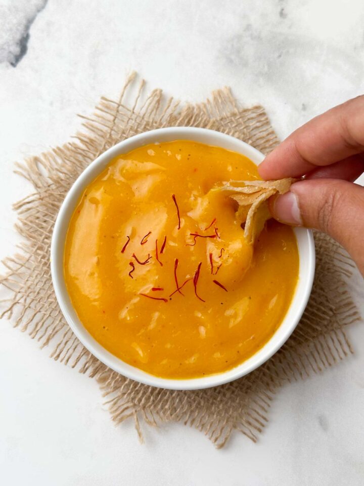 aamras served in a bowl garnished with saffron with poori in the hand