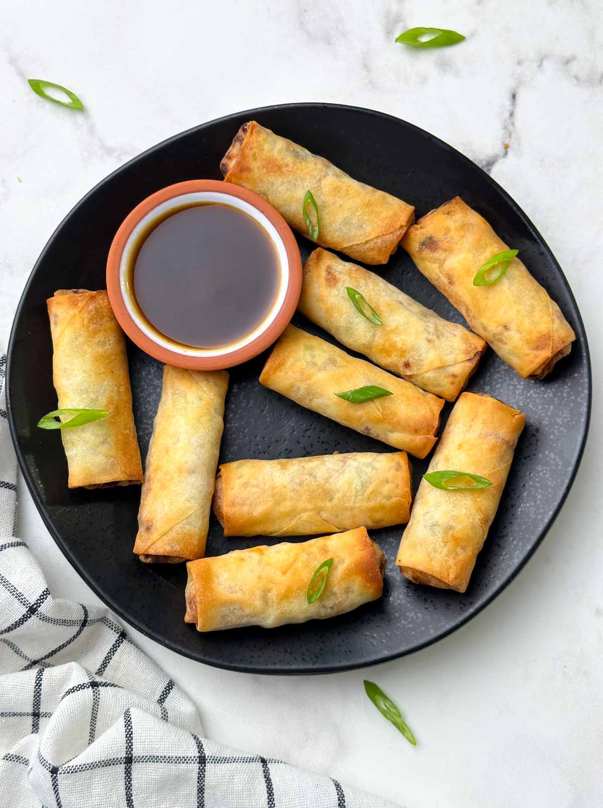 air fryer frozen spring rolls served on the plate with soy ginger sauce garnished with green spring onions