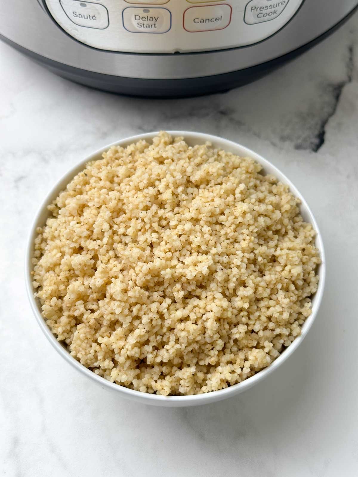 cooked millet in a bowl with instant pot behind