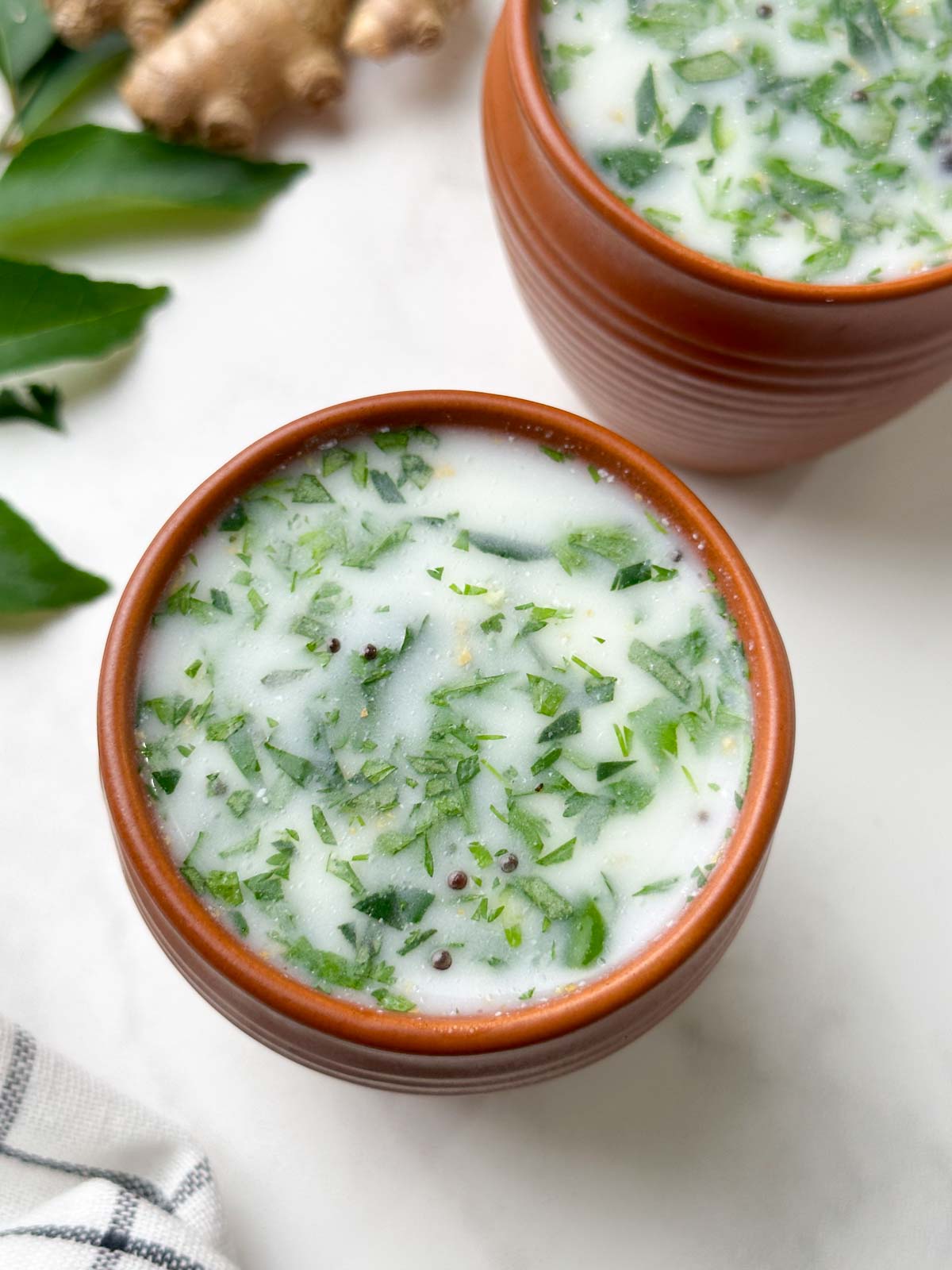 neer mor (neer majjige) served in a serving glass with curry leaves and ginger on the side