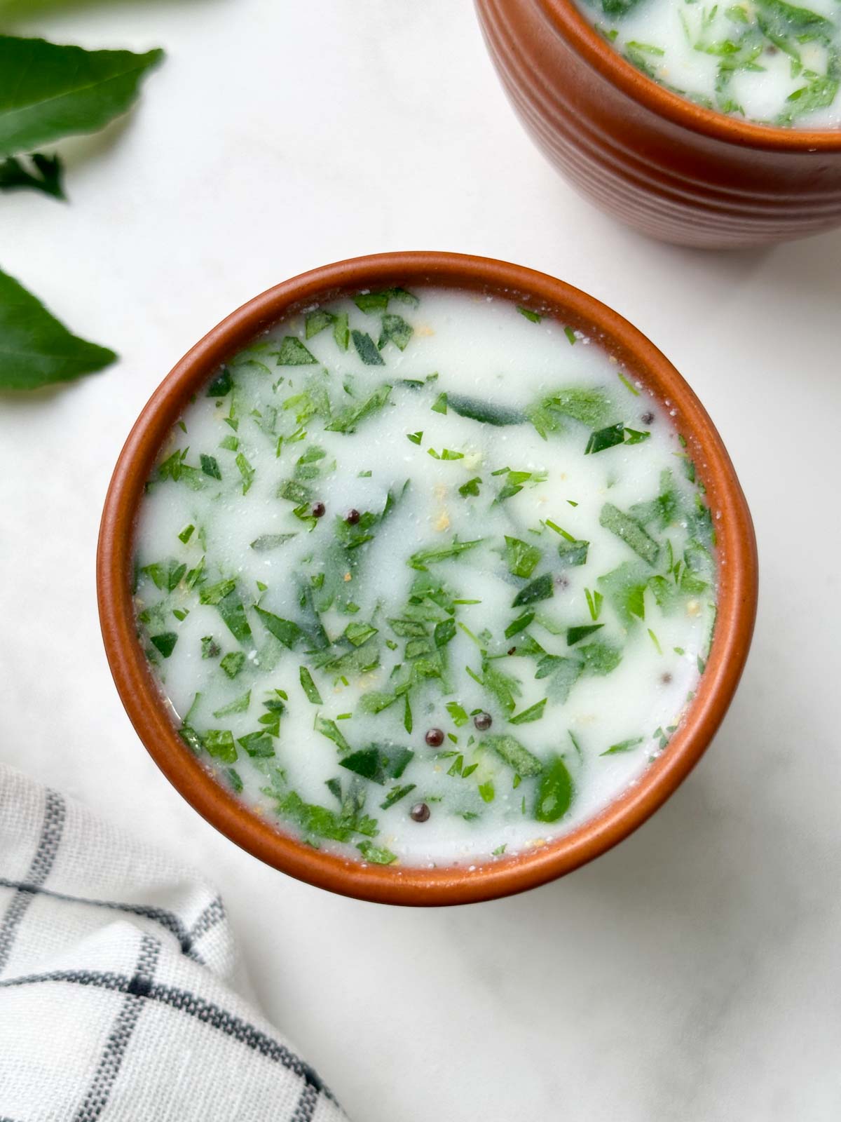 neer mor (neer majjige) served in a serving glass with curry leaves and ginger on the side