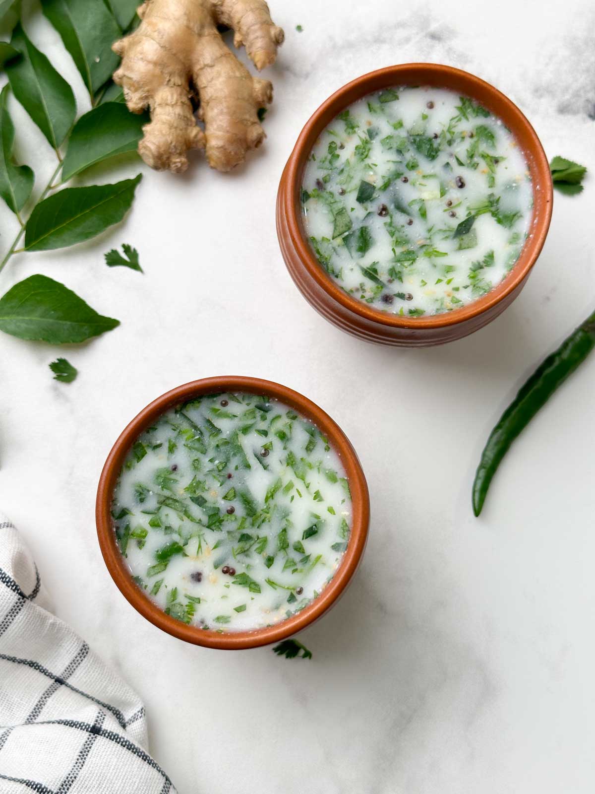 2 glasses of majjige served with curry leaves, ginger root on the side