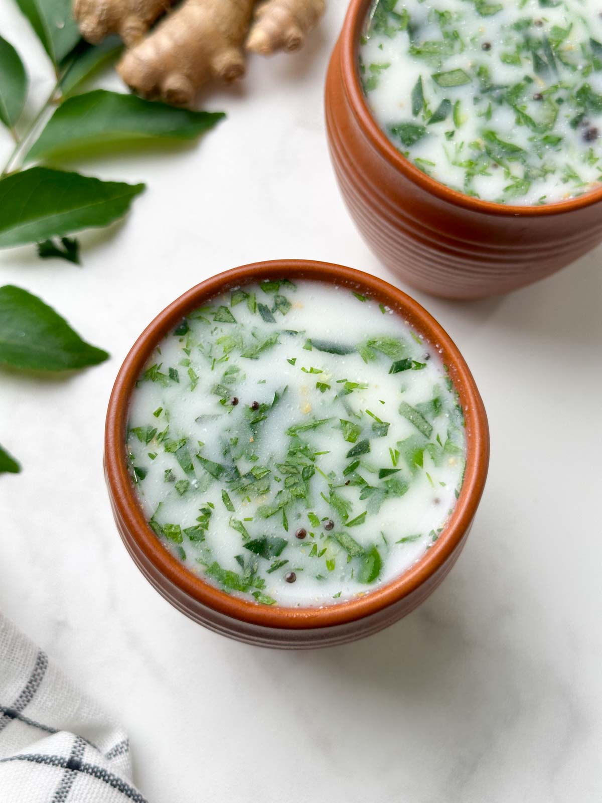 neer mor served in a serving glass with curry leaves and ginger on the side