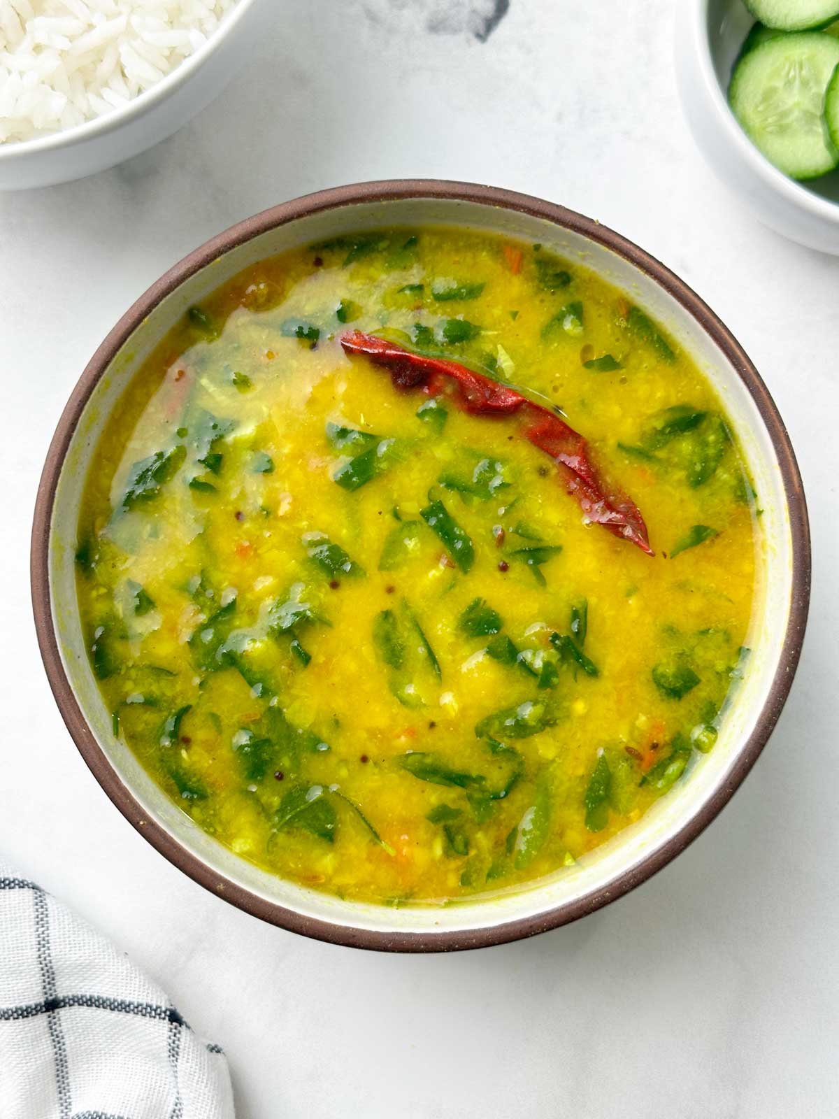 fenugreek leaves dal served in a bowl with rice and cucumber on the side