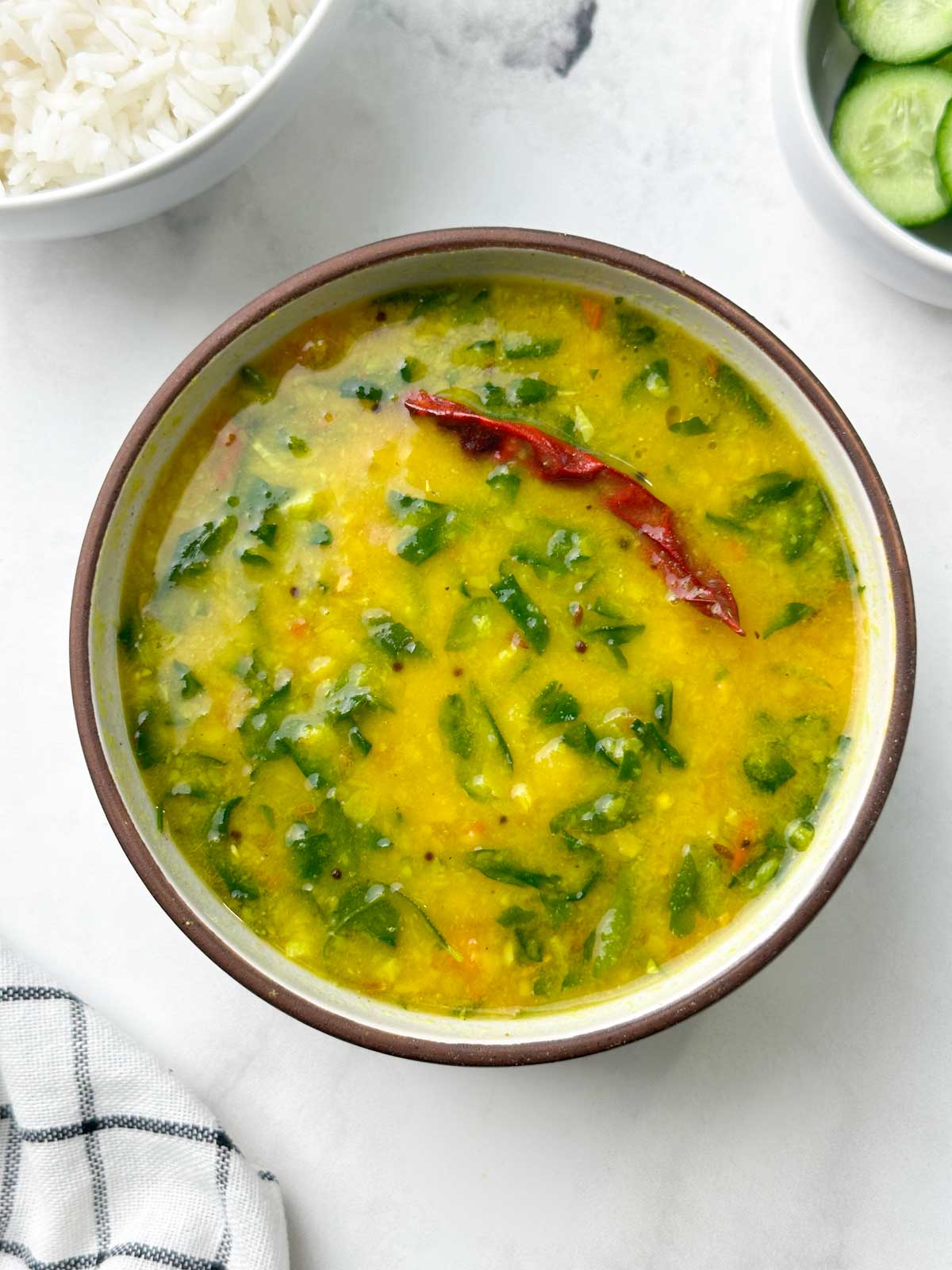 Dal methi served in a bowl with rice and cucumber salad on the side